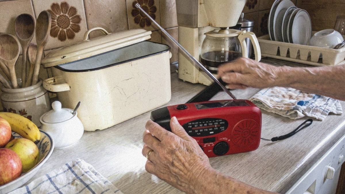 Hände an der ausgeklappten Kurbel des roten Radios, Antenne ausgezogen