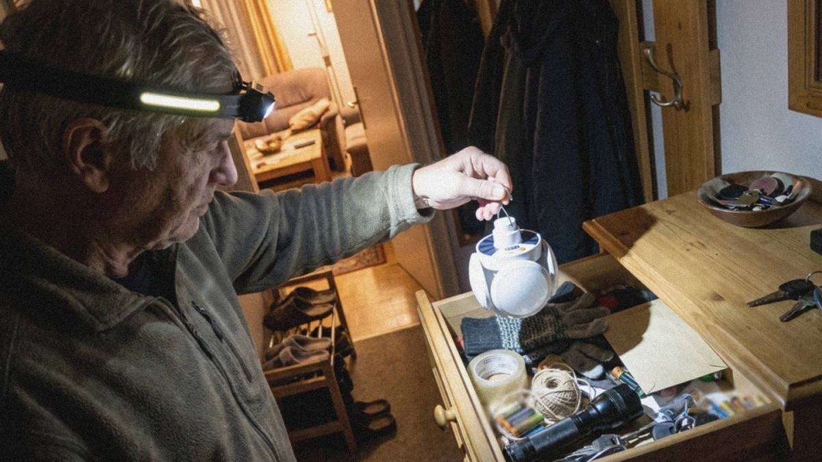 Person mit Stirnlampe im dunklen Flur vor dem Sicherungskasten, beide Hände frei